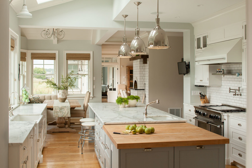 Photo of a large beach style u-shaped eat-in kitchen in New York with a farmhouse sink, recessed-panel cabinets, white cabinets, marble benchtops, white splashback, stainless steel appliances, light hardwood floors and with island.
