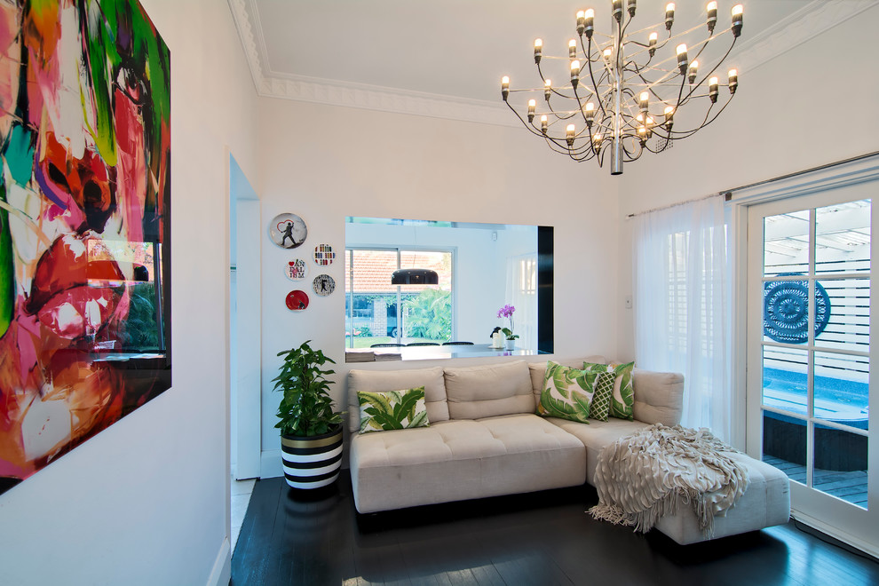 Imagen de sala de estar tropical pequeña sin chimenea y televisor con paredes blancas, suelo de madera oscura y suelo negro