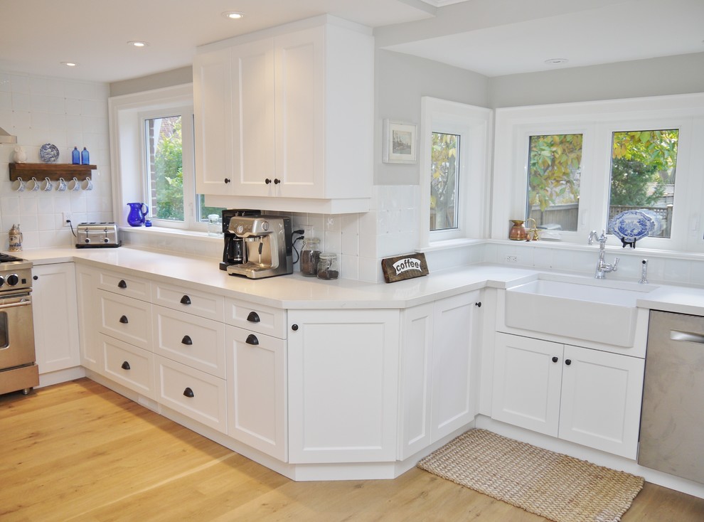 Eat-in kitchen - small transitional l-shaped light wood floor eat-in kitchen idea in Toronto with a farmhouse sink, shaker cabinets, white cabinets, quartz countertops, white backsplash, ceramic backsplash, stainless steel appliances and a peninsula
