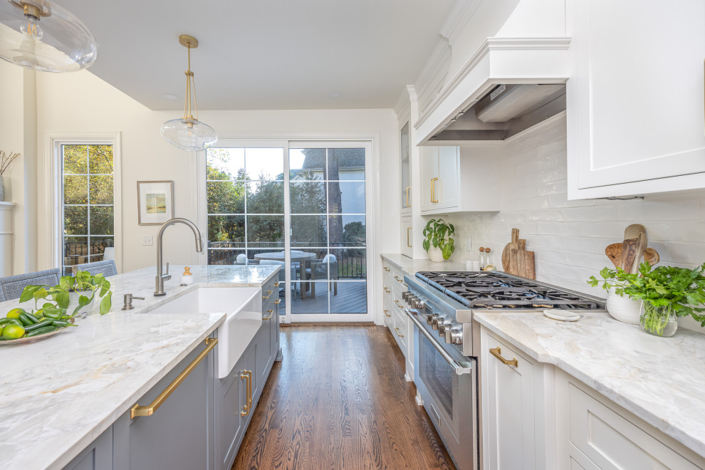 Mid-sized transitional open plan kitchen in Raleigh with a farmhouse sink, shaker cabinets, white cabinets, quartzite benchtops, white splashback, subway tile splashback, stainless steel appliances, medium hardwood floors, with island, brown floor and multi-coloured benchtop.