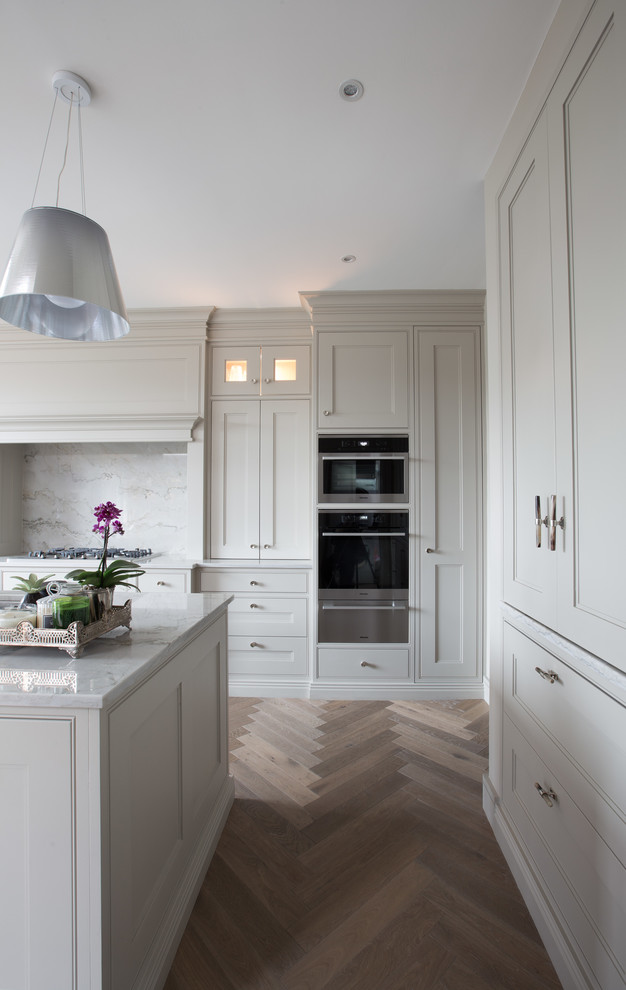 Contemporary l-shaped open plan kitchen in Dublin with shaker cabinets, grey cabinets, marble benchtops, stone slab splashback, medium hardwood floors and with island.