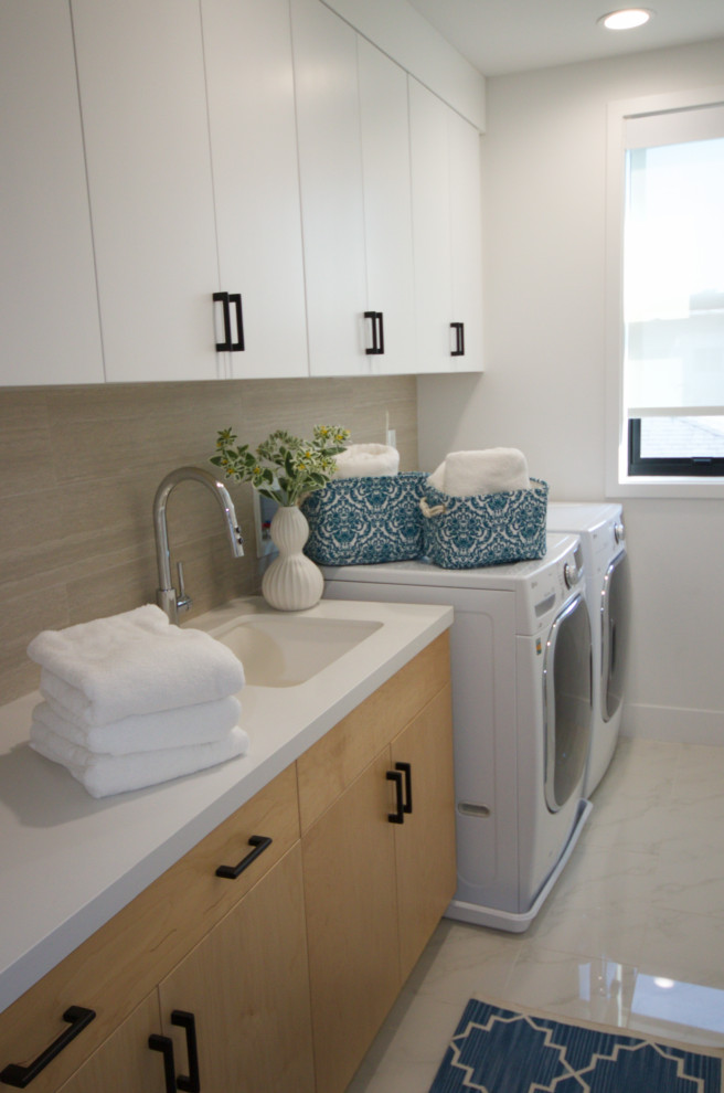Inspiration for a large modern galley dedicated laundry room in Los Angeles with an undermount sink, flat-panel cabinets, white cabinets, quartz benchtops, beige splashback, porcelain splashback, white walls, marble floors, a side-by-side washer and dryer, white floor and white benchtop.