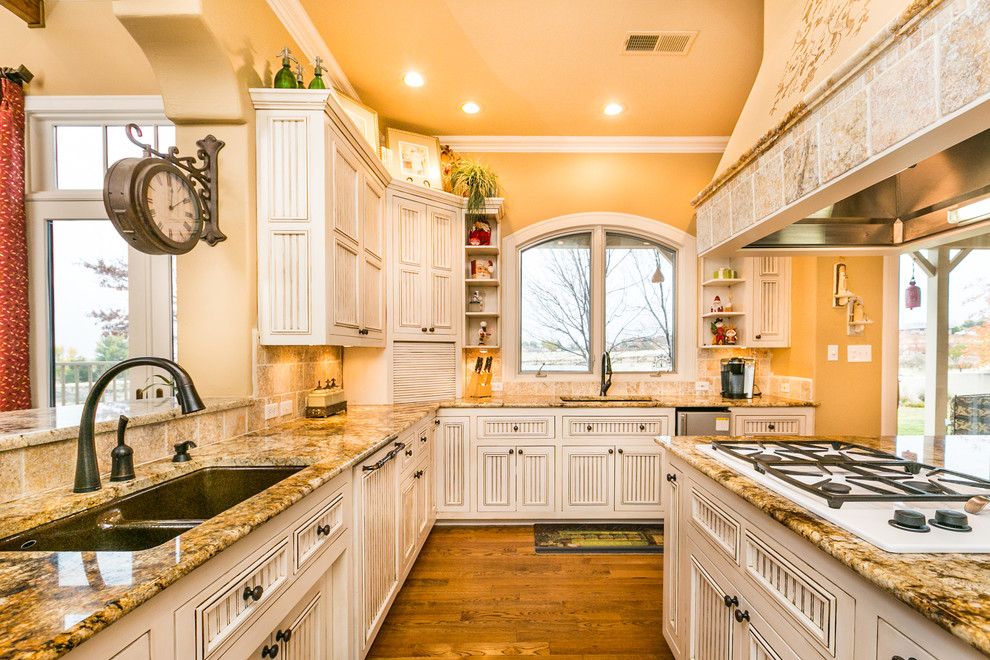 This is an example of a large traditional u-shaped eat-in kitchen in Albuquerque with an undermount sink, white cabinets, granite benchtops, beige splashback, stone tile splashback, medium hardwood floors, with island, louvered cabinets and white appliances.