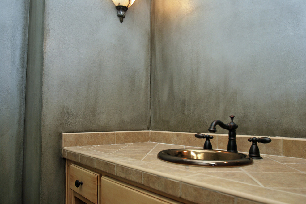 Photo of a small mediterranean bathroom in Kansas City with a drop-in sink, recessed-panel cabinets, distressed cabinets, tile benchtops, brown tile, porcelain tile and grey walls.