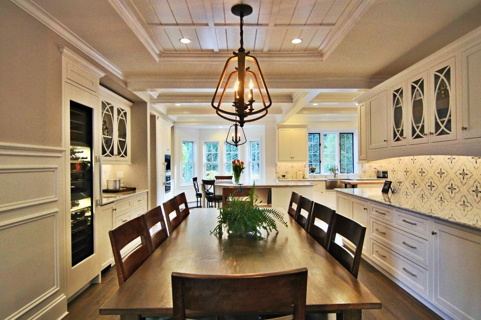 Example of a large transitional l-shaped laminate floor and brown floor open concept kitchen design in Boston with a farmhouse sink, recessed-panel cabinets, white cabinets, marble countertops, white backsplash, marble backsplash, paneled appliances and an island