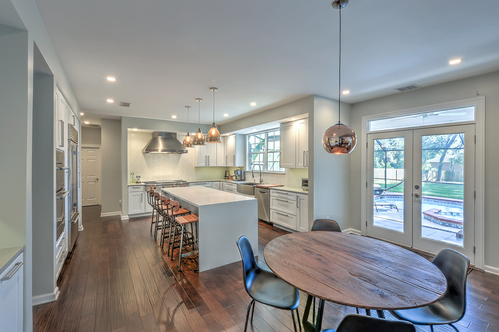 Design ideas for a large transitional u-shaped eat-in kitchen in Jacksonville with a farmhouse sink, recessed-panel cabinets, white cabinets, quartzite benchtops, white splashback, ceramic splashback, stainless steel appliances, dark hardwood floors, with island and brown floor.