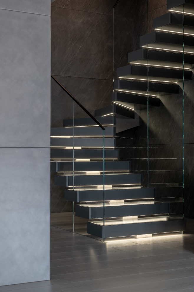 Ejemplo de escalera en U moderna de tamaño medio con escalones de metal, contrahuellas de hormigón, barandilla de vidrio y boiserie