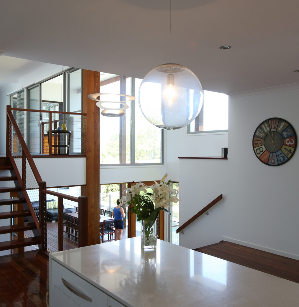 Photo of a tropical kitchen in Brisbane with flat-panel cabinets, white cabinets, quartz benchtops, medium hardwood floors, with island and white benchtop.