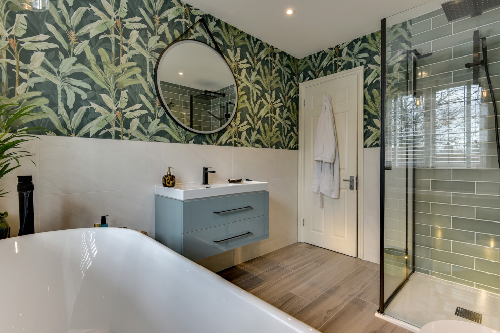 Inspiration for a medium sized grey and white family bathroom in Sussex with flat-panel cabinets, blue cabinets, a freestanding bath, a walk-in shower, a one-piece toilet, green tiles, ceramic tiles, green walls, light hardwood flooring, a built-in sink, brown floors, a hinged door, white worktops, feature lighting, a single sink, a floating vanity unit and wallpapered walls.