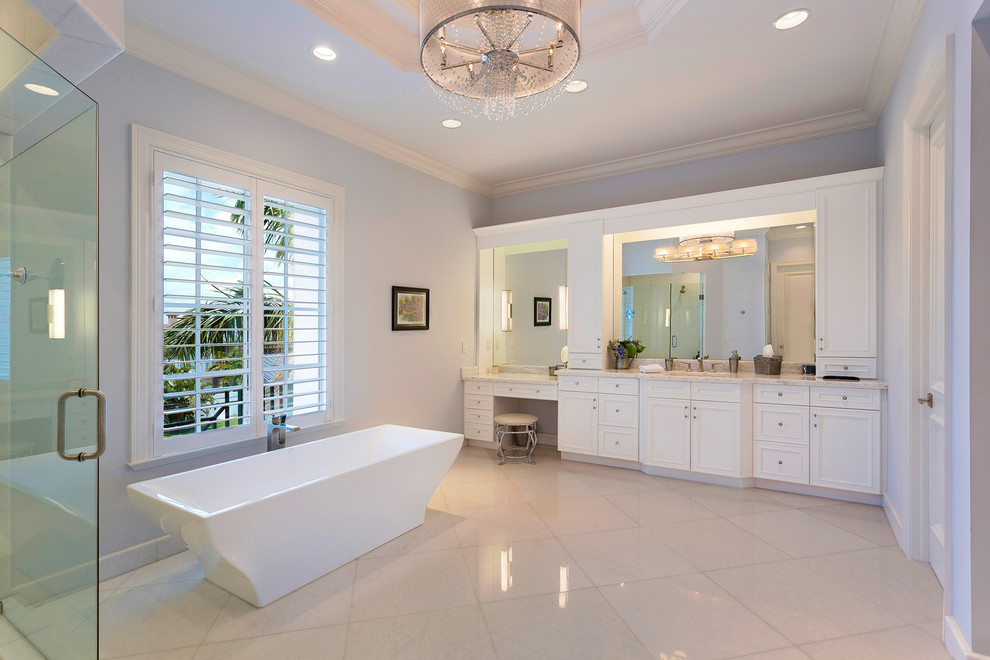 Expansive tropical master bathroom in Other with recessed-panel cabinets, white cabinets, a freestanding tub, an alcove shower, a one-piece toilet, gray tile, marble, white walls, an undermount sink, marble benchtops, a hinged shower door, grey benchtops, porcelain floors and beige floor.