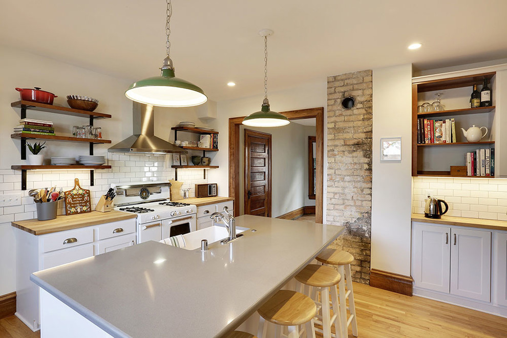 Inspiration for a contemporary galley kitchen in Minneapolis with a farmhouse sink, shaker cabinets, white cabinets, white splashback, subway tile splashback, white appliances, medium hardwood floors, with island and brown floor.