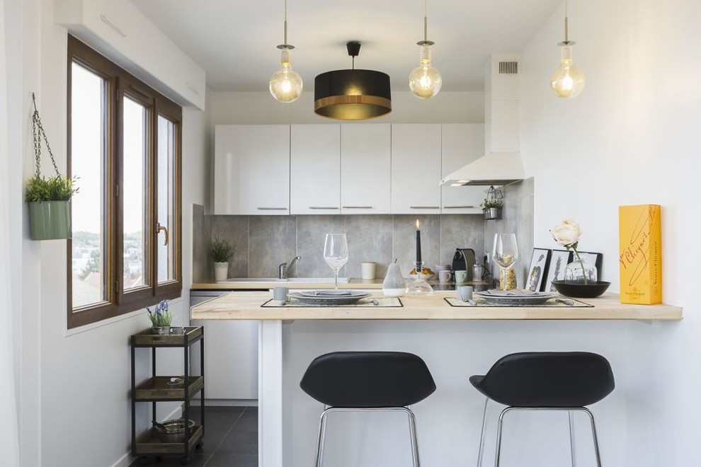 Inspiration for a scandinavian kitchen in Other with a drop-in sink, flat-panel cabinets, white cabinets, wood benchtops, grey splashback, a peninsula, black floor and beige benchtop.