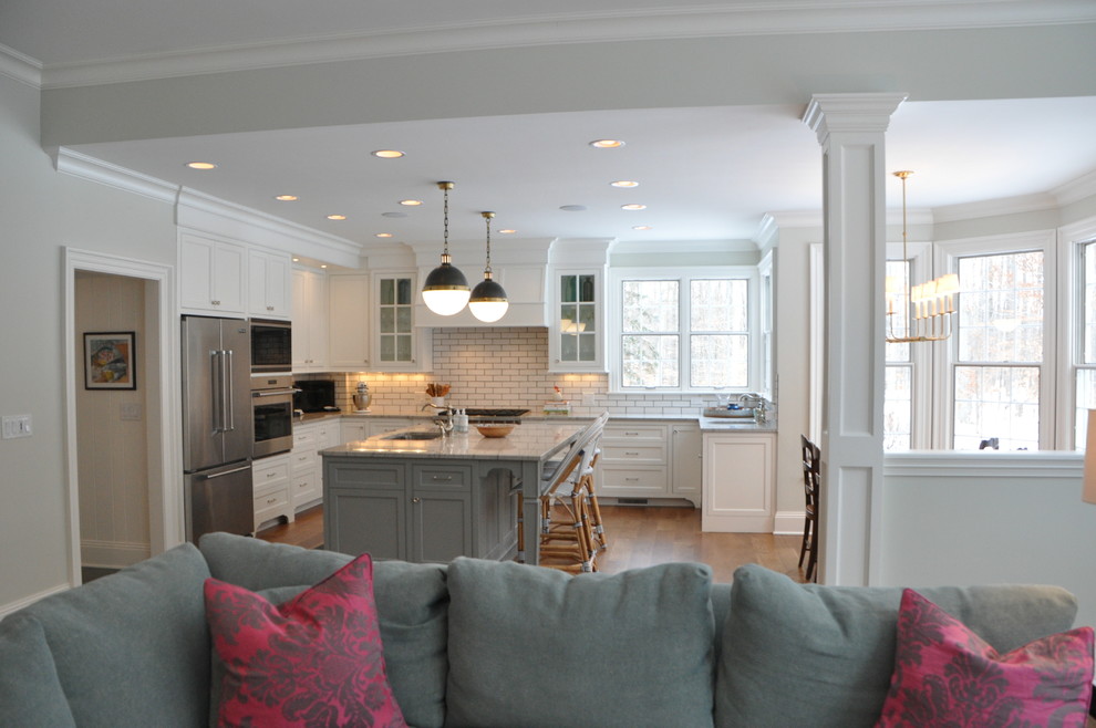 Open concept kitchen - large transitional l-shaped medium tone wood floor and brown floor open concept kitchen idea in Cleveland with an undermount sink, recessed-panel cabinets, white cabinets, marble countertops, white backsplash, subway tile backsplash, stainless steel appliances, an island and white countertops
