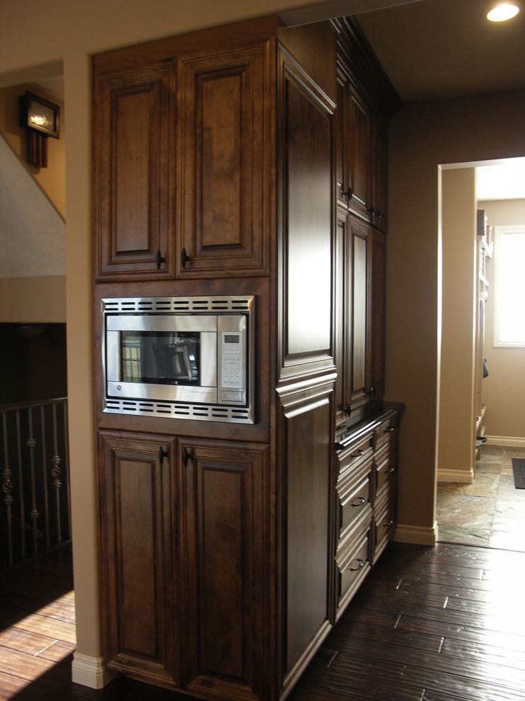 This is an example of a mid-sized traditional l-shaped eat-in kitchen in Edmonton with an undermount sink, raised-panel cabinets, granite benchtops, brown splashback, stone tile splashback, stainless steel appliances, medium wood cabinets, dark hardwood floors, with island and brown floor.