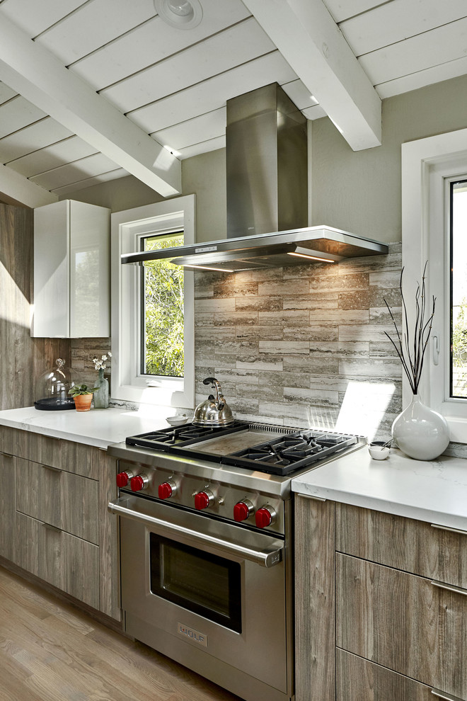 Inspiration for a large contemporary l-shaped open plan kitchen in San Francisco with an undermount sink, flat-panel cabinets, grey cabinets, quartz benchtops, grey splashback, travertine splashback, stainless steel appliances, light hardwood floors, with island, brown floor and grey benchtop.