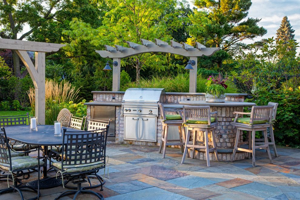 Réalisation d'une grande terrasse arrière tradition avec des pavés en pierre naturelle et une pergola.