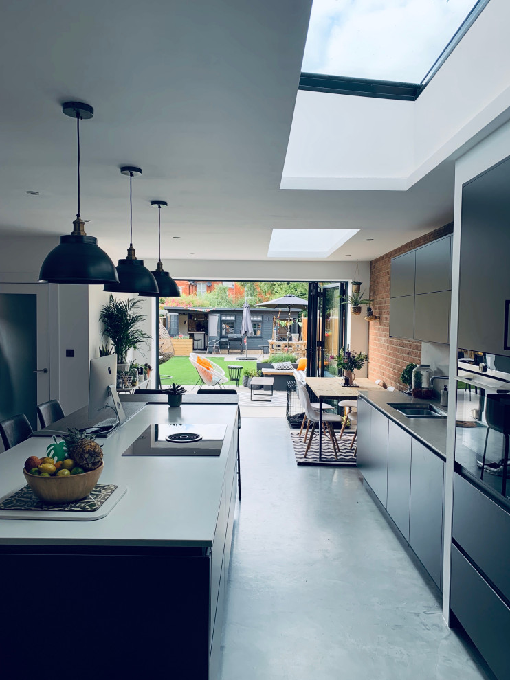 Mid-sized contemporary u-shaped open plan kitchen in Berkshire with a drop-in sink, flat-panel cabinets, black cabinets, tile benchtops, grey splashback, ceramic splashback, black appliances, concrete floors, with island, grey floor, grey benchtop and coffered.