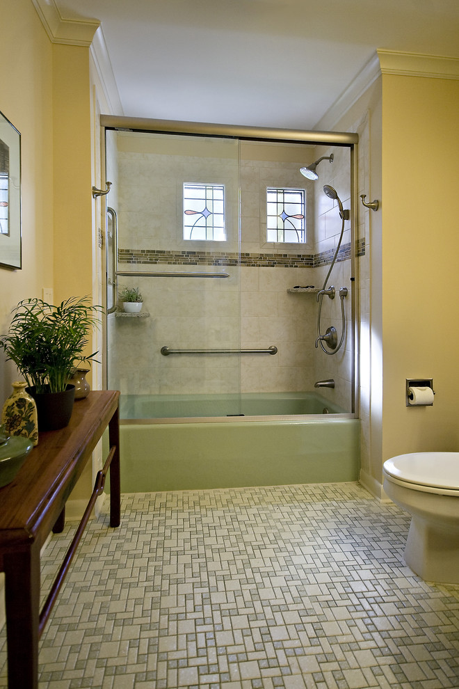 This is an example of a mid-sized transitional kids bathroom in Raleigh with an undermount sink, raised-panel cabinets, medium wood cabinets, engineered quartz benchtops, an alcove tub, an alcove shower, a two-piece toilet, beige tile, ceramic tile, yellow walls, ceramic floors, multi-coloured floor, a sliding shower screen and beige benchtops.