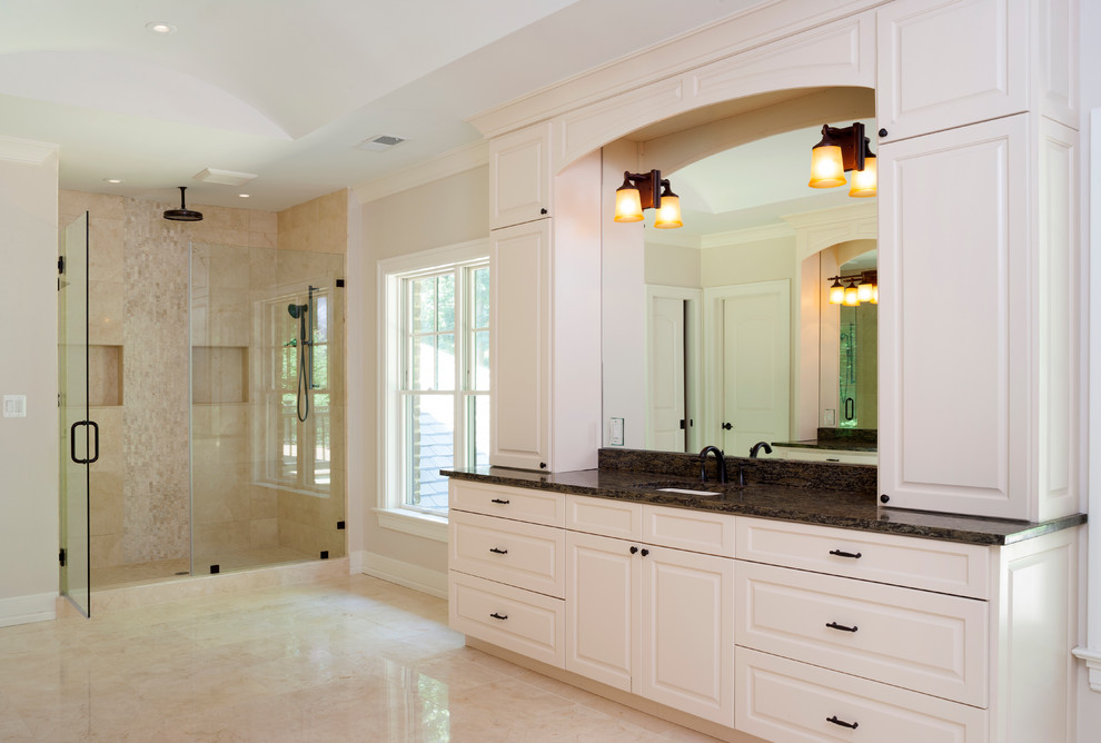 Example of a large transitional master beige tile and limestone tile limestone floor and beige floor corner shower design in DC Metro with raised-panel cabinets, white cabinets, a one-piece toilet, beige walls, an undermount sink, granite countertops and a hinged shower door