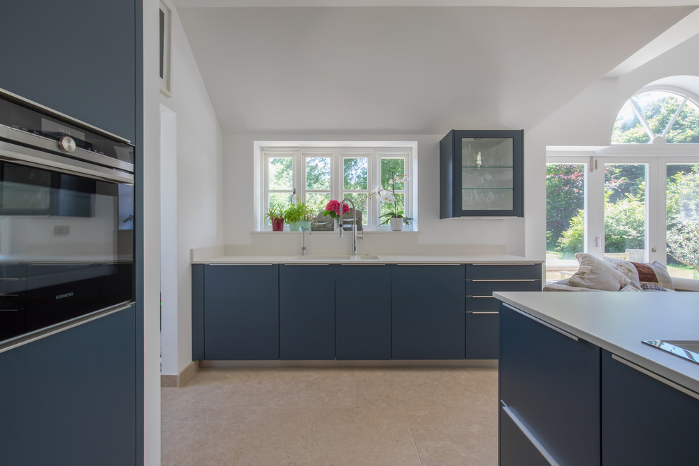 Design ideas for a large contemporary open plan kitchen in Sussex with an integrated sink, flat-panel cabinets, blue cabinets, quartz benchtops, stainless steel appliances, limestone floors, with island and beige floor.