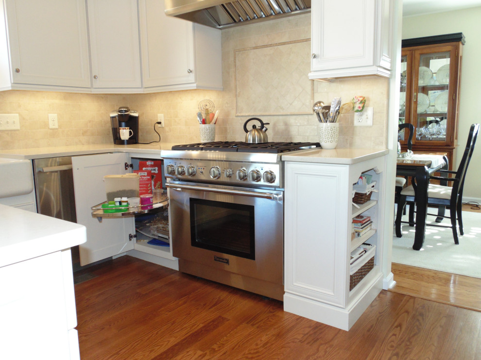 Inspiration for a large transitional u-shaped medium tone wood floor and brown floor eat-in kitchen remodel with a farmhouse sink, flat-panel cabinets, white cabinets, quartz countertops, beige backsplash, travertine backsplash, stainless steel appliances and beige countertops