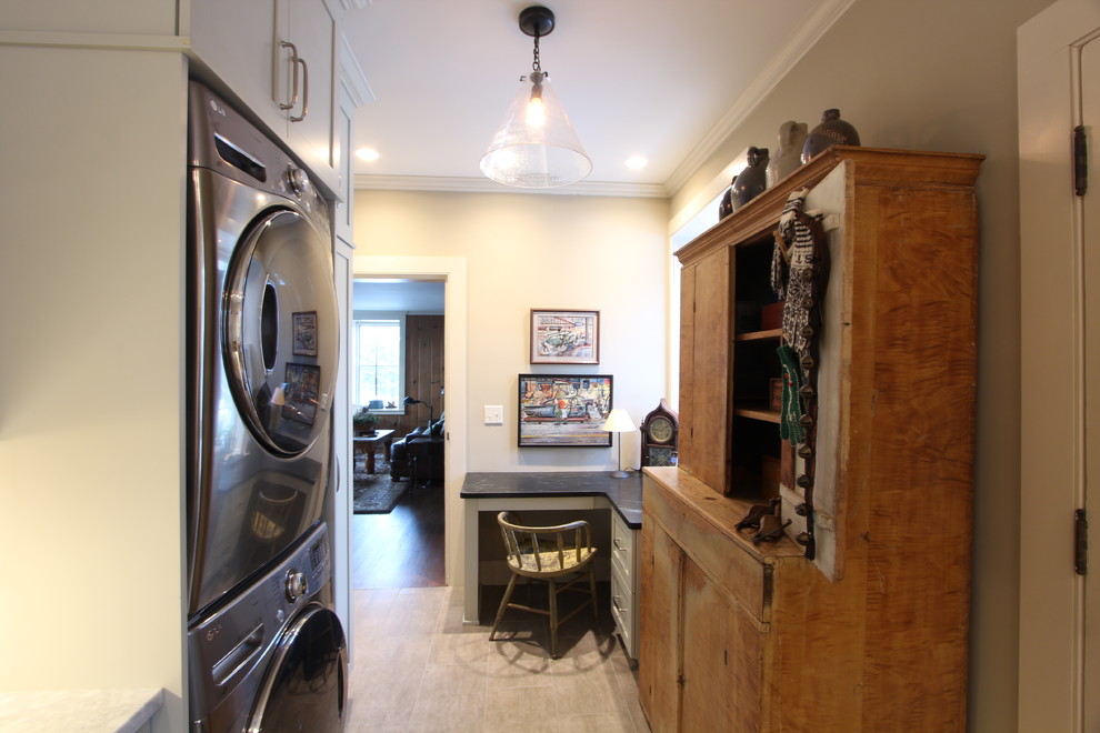 This is an example of a mid-sized country galley utility room in Other with a farmhouse sink, recessed-panel cabinets, green cabinets, granite benchtops, beige walls, porcelain floors, a stacked washer and dryer, brown floor and green benchtop.