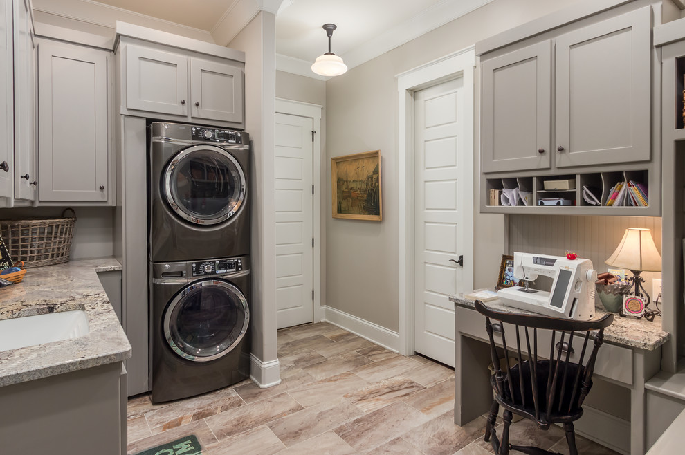 Design ideas for a mid-sized country u-shaped dedicated laundry room in Nashville with an undermount sink, recessed-panel cabinets, grey cabinets, granite benchtops, a stacked washer and dryer and beige walls.