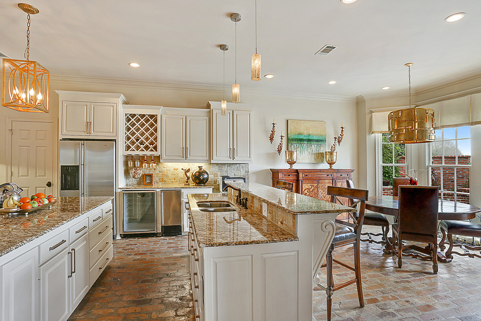 Inspiration for a large transitional u-shaped open plan kitchen in New Orleans with a drop-in sink, raised-panel cabinets, white cabinets, granite benchtops, beige splashback, stone tile splashback, stainless steel appliances, brick floors and with island.