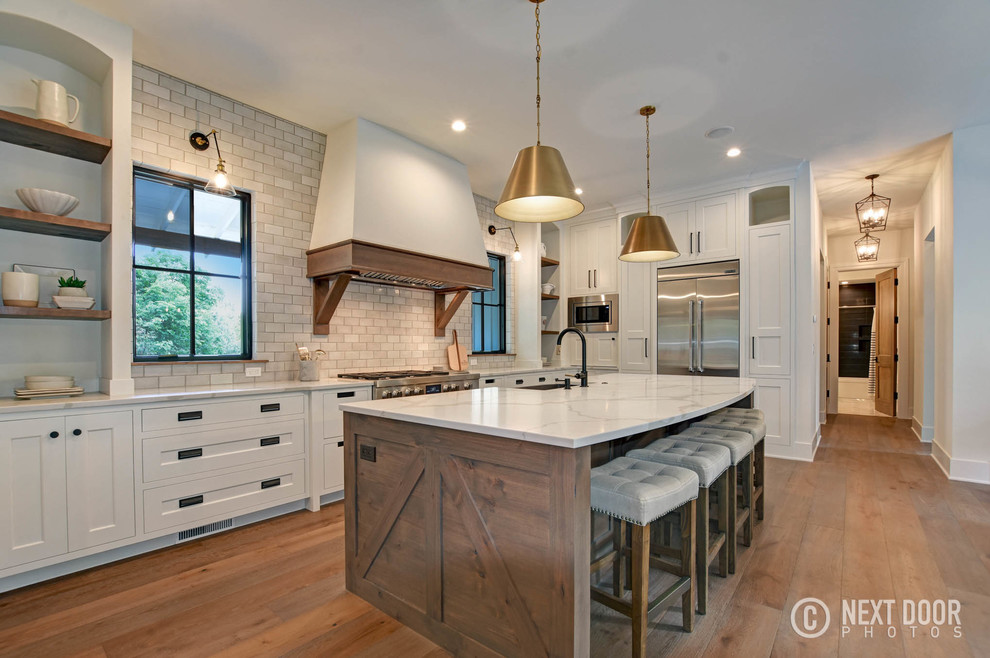 Large country l-shaped eat-in kitchen in Grand Rapids with a farmhouse sink, beaded inset cabinets, white cabinets, quartz benchtops, grey splashback, terra-cotta splashback, stainless steel appliances, medium hardwood floors, with island, beige floor and white benchtop.