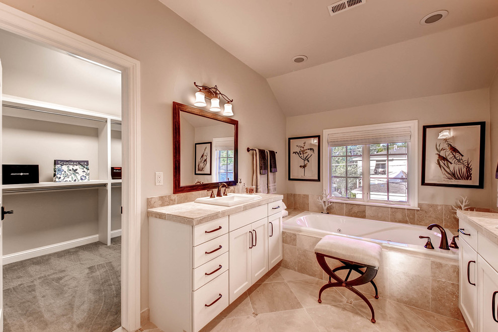 Mid-sized transitional master bathroom in Denver with a drop-in sink, shaker cabinets, white cabinets, tile benchtops, a drop-in tub, a double shower, a two-piece toilet, beige tile, stone tile, grey walls and travertine floors.