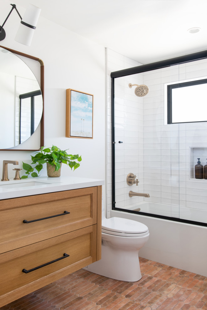 Medium sized mediterranean family bathroom in Los Angeles with a floating vanity unit, recessed-panel cabinets, brown cabinets, an alcove bath, a shower/bath combination, a one-piece toilet, white tiles, marble tiles, white walls, terracotta flooring, a wall-mounted sink, marble worktops, orange floors, a sliding door, white worktops and a single sink.