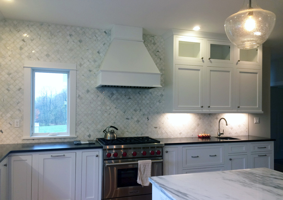 Kitchen pantry - large transitional l-shaped dark wood floor and brown floor kitchen pantry idea with a farmhouse sink, recessed-panel cabinets, white cabinets, quartz countertops, beige backsplash, ceramic backsplash, stainless steel appliances, an island and black countertops