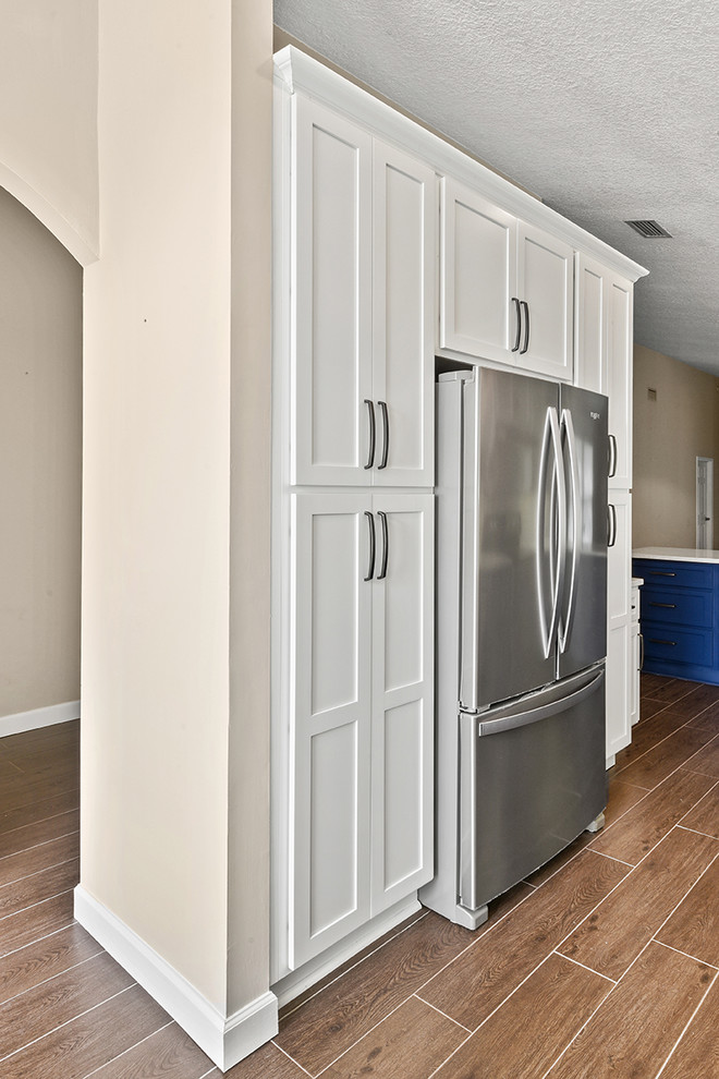 Inspiration for a large transitional l-shaped vinyl floor and brown floor open concept kitchen remodel in Jacksonville with an undermount sink, shaker cabinets, blue cabinets, quartzite countertops, white backsplash, ceramic backsplash, stainless steel appliances and a peninsula