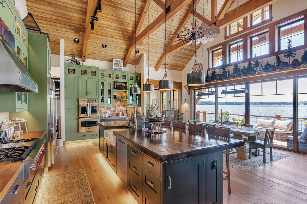 Open concept kitchen - mid-sized rustic u-shaped medium tone wood floor, brown floor and vaulted ceiling open concept kitchen idea in Seattle with a farmhouse sink, recessed-panel cabinets, green cabinets, soapstone countertops, white backsplash, porcelain backsplash, stainless steel appliances, an island and black countertops