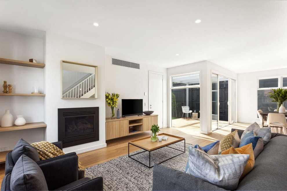 Transitional living room in Melbourne with white walls, medium hardwood floors, a standard fireplace, a freestanding tv and brown floor.
