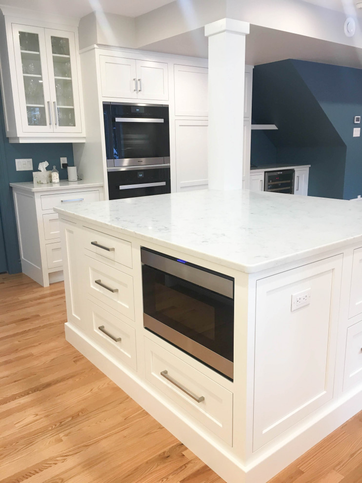 Eat-in kitchen - large transitional u-shaped light wood floor and beige floor eat-in kitchen idea with a double-bowl sink, shaker cabinets, white cabinets, quartzite countertops, white backsplash, subway tile backsplash, stainless steel appliances, an island and white countertops