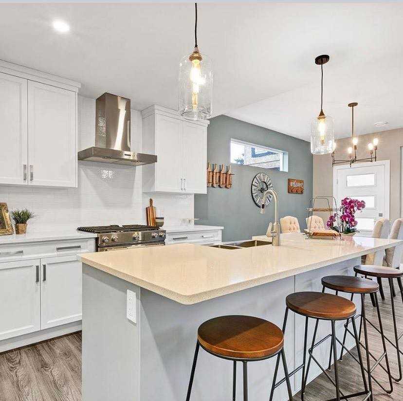 Mid-sized contemporary l-shaped eat-in kitchen in Vancouver with with island, a double-bowl sink, recessed-panel cabinets, white cabinets, solid surface benchtops, white splashback, subway tile splashback, stainless steel appliances, light hardwood floors, grey floor and white benchtop.