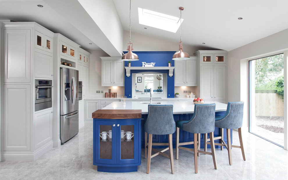Design ideas for an expansive transitional l-shaped open plan kitchen in Dublin with an integrated sink, louvered cabinets, blue cabinets, quartzite benchtops, white splashback, stone slab splashback, stainless steel appliances, ceramic floors and with island.