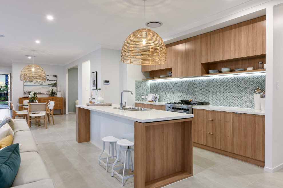 This is an example of a contemporary galley kitchen in Brisbane with a drop-in sink, flat-panel cabinets, medium wood cabinets, blue splashback, mosaic tile splashback, stainless steel appliances, with island, grey floor and white benchtop.