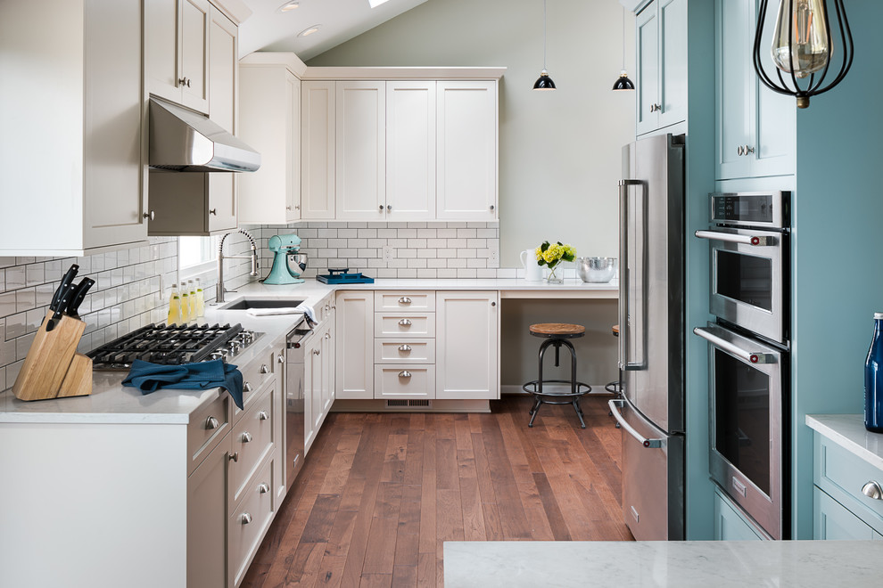 Inspiration for a large transitional l-shaped medium tone wood floor kitchen remodel in New York with an undermount sink, flat-panel cabinets, blue cabinets, quartz countertops, white backsplash, ceramic backsplash, stainless steel appliances and a peninsula