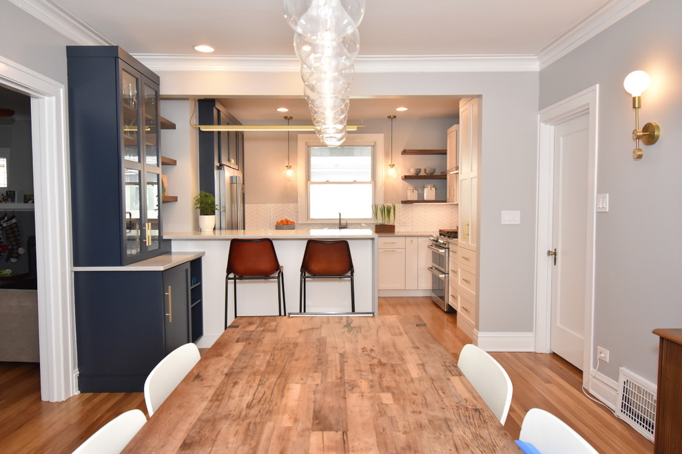 Example of a mid-sized trendy u-shaped medium tone wood floor and brown floor eat-in kitchen design in Chicago with shaker cabinets, blue cabinets, quartz countertops, white backsplash, ceramic backsplash, stainless steel appliances, a peninsula and gray countertops