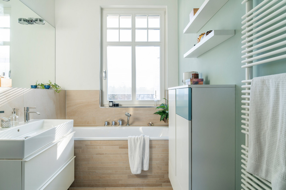 Badezimmer With türkisfarbenen Schränken, Einbaubadewanne, Wandtoilette, beigen Fliesen and integriertem Waschbecken in Berlin