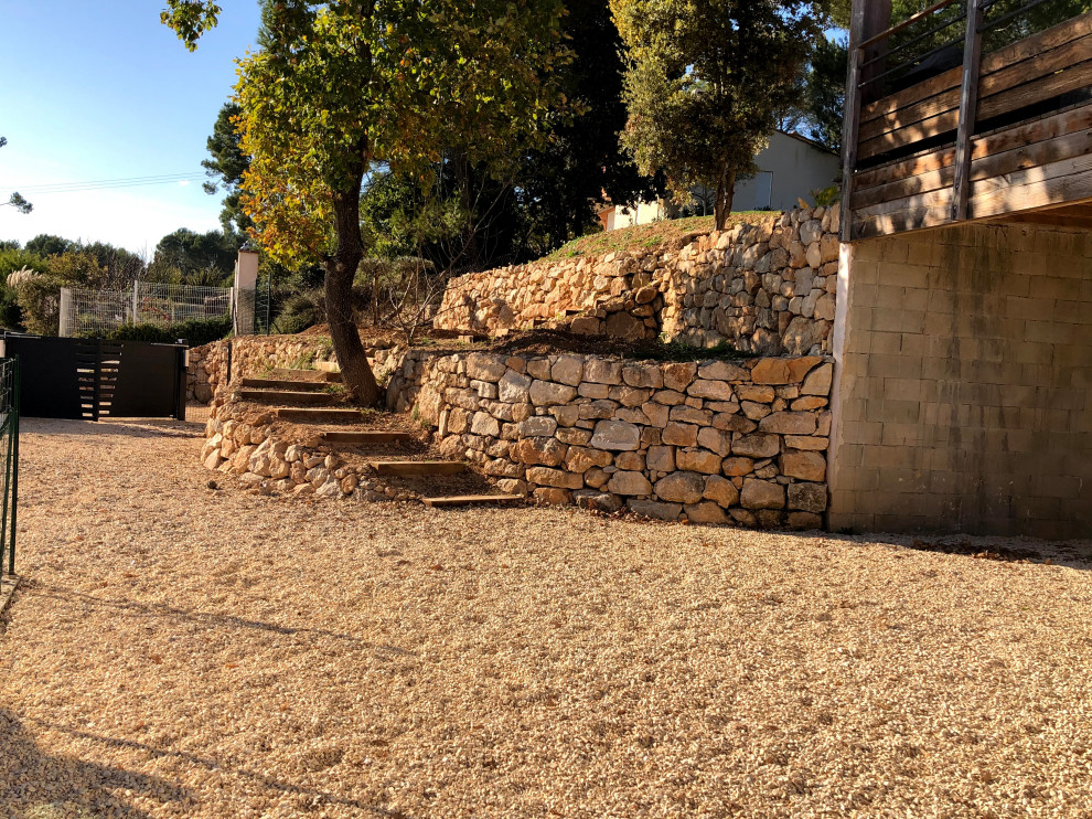Exemple d'un grand jardin chic avec un mur de soutènement, une pente, une colline ou un talus et une clôture en pierre.