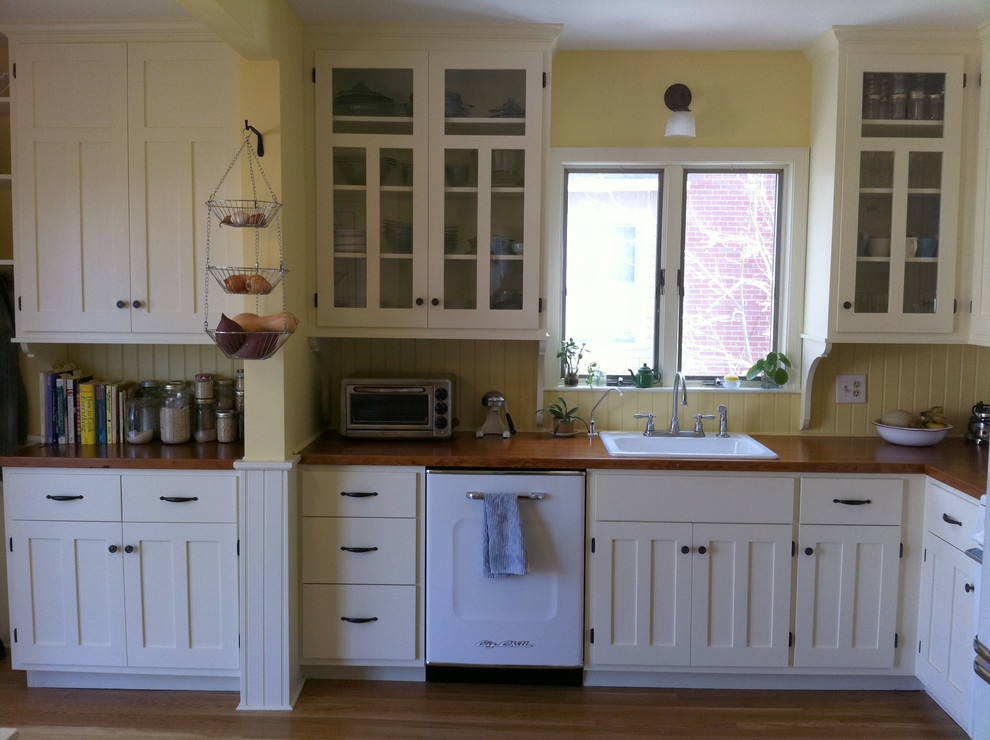 This is an example of a country l-shaped separate kitchen in Providence with a drop-in sink, recessed-panel cabinets, white cabinets, wood benchtops, yellow splashback, white appliances and medium hardwood floors.