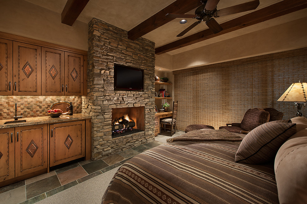 This is an example of a mid-sized guest bedroom in Phoenix with beige walls, slate floors, a standard fireplace and a stone fireplace surround.