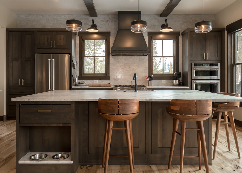 Inspiration for a large rustic l-shaped light wood floor and beige floor open concept kitchen remodel in Denver with an undermount sink, shaker cabinets, dark wood cabinets, quartz countertops, beige backsplash, subway tile backsplash, stainless steel appliances, an island and white countertops