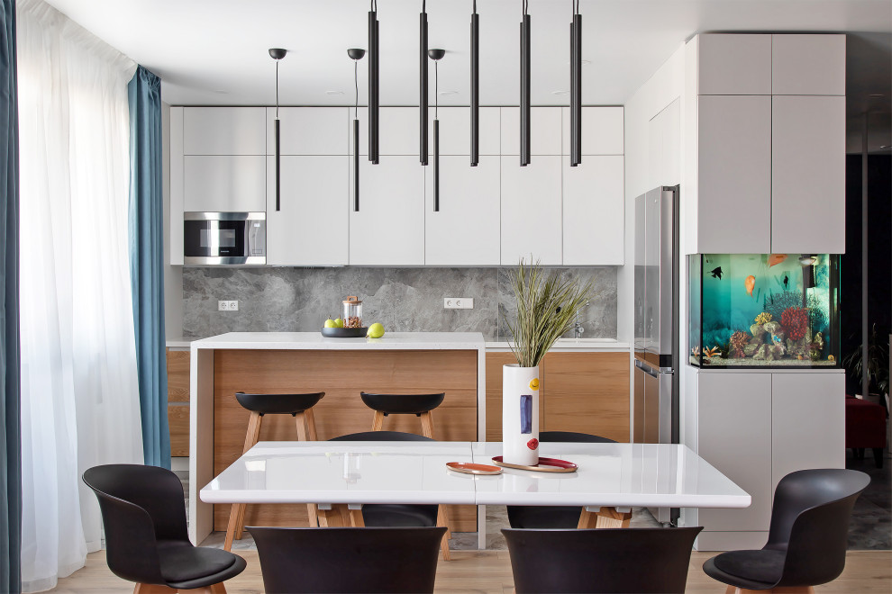 Inspiration for a mid-sized contemporary single-wall open plan kitchen in Other with an integrated sink, flat-panel cabinets, light wood cabinets, solid surface benchtops, grey splashback, porcelain splashback, stainless steel appliances, porcelain floors, with island, grey floor and white benchtop.