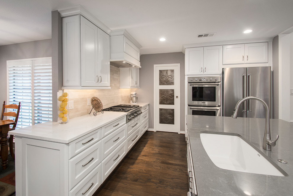 Design ideas for a mid-sized transitional l-shaped open plan kitchen in Dallas with an undermount sink, flat-panel cabinets, white cabinets, quartz benchtops, beige splashback, ceramic splashback, stainless steel appliances, medium hardwood floors, with island and brown floor.