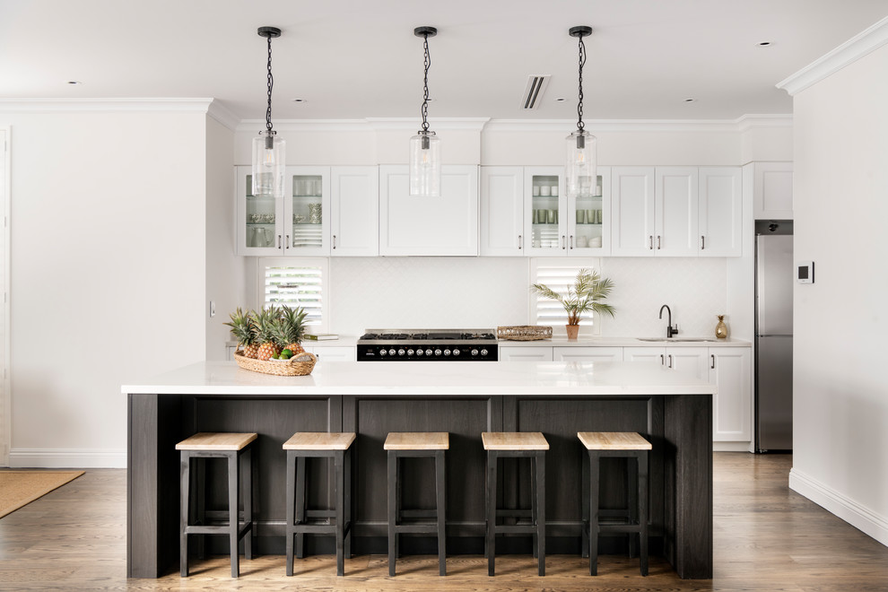 Inspiration for a large transitional single-wall kitchen in Perth with a double-bowl sink, shaker cabinets, white splashback, black appliances, medium hardwood floors, with island, brown floor and white benchtop.