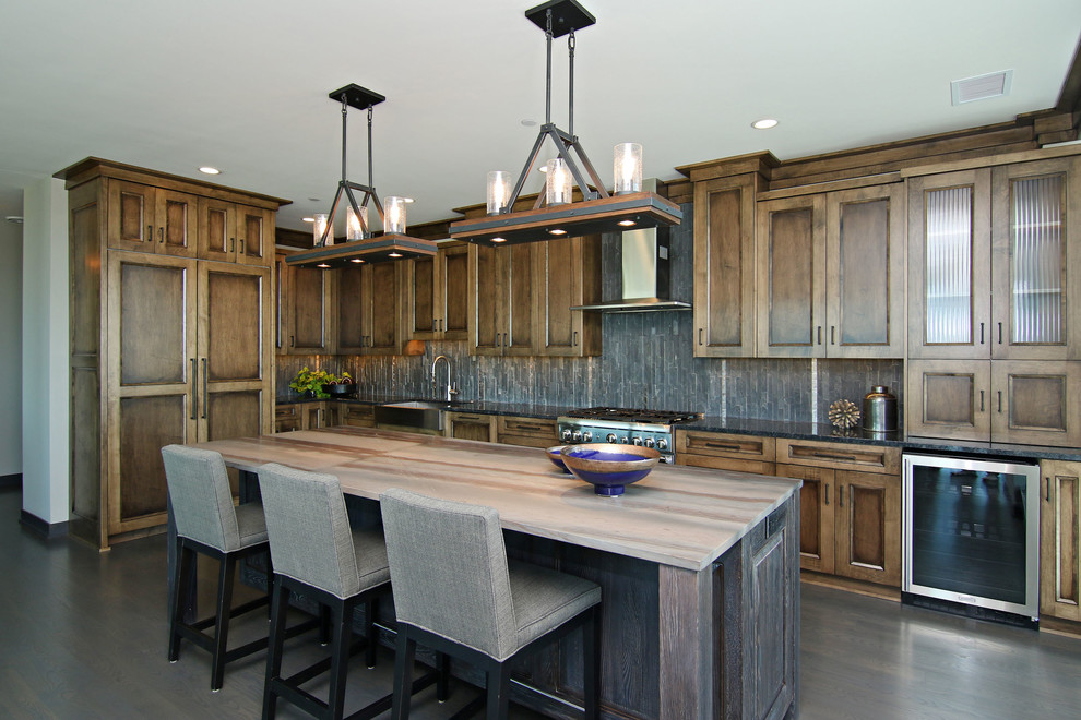 Inspiration for a large industrial l-shaped eat-in kitchen in Minneapolis with a farmhouse sink, recessed-panel cabinets, dark wood cabinets, granite benchtops, black splashback, stone tile splashback, stainless steel appliances, dark hardwood floors and with island.